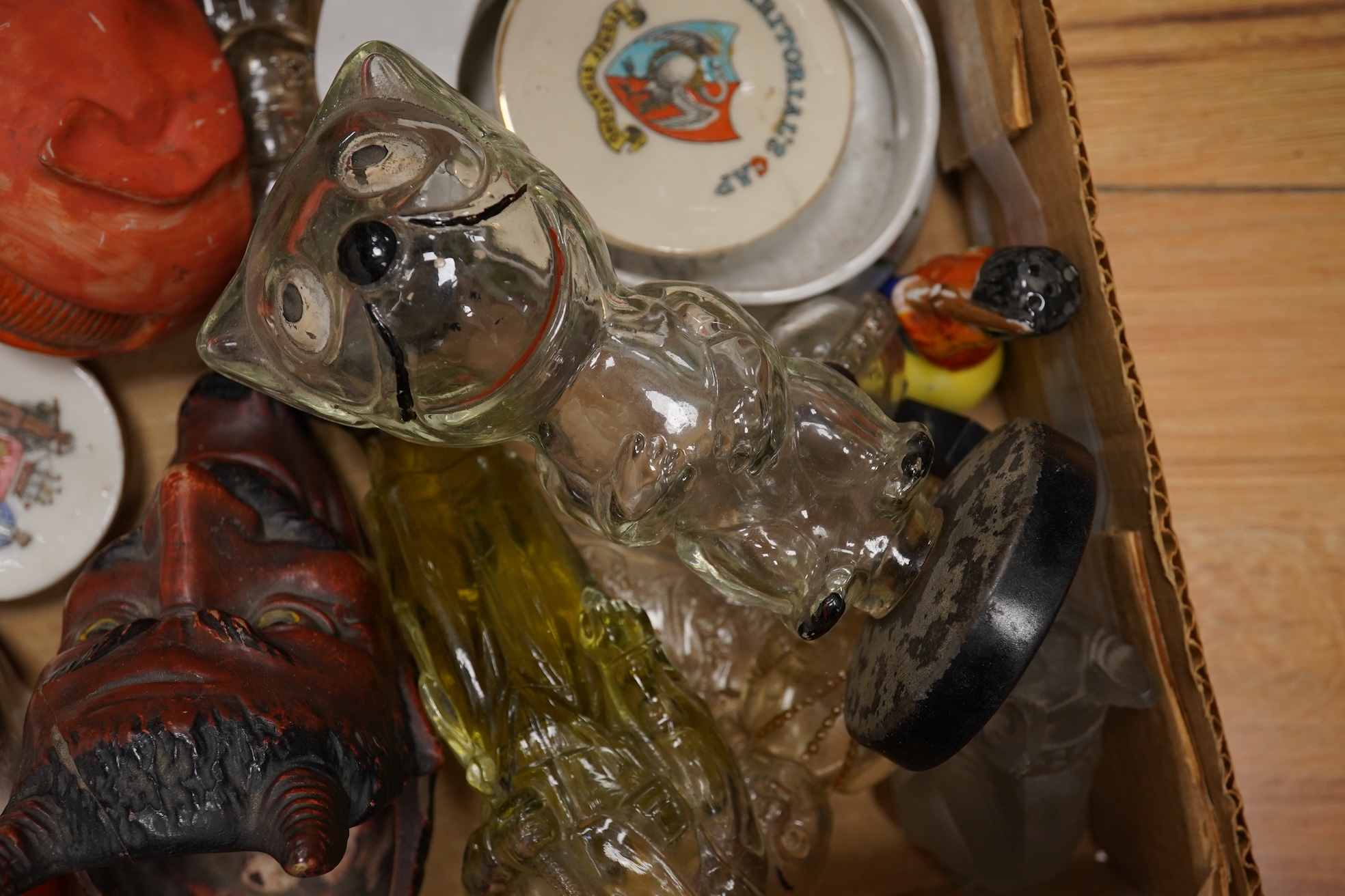 A collection of sundry items to include novelty glass bottles, devil pots and ceramic military caps